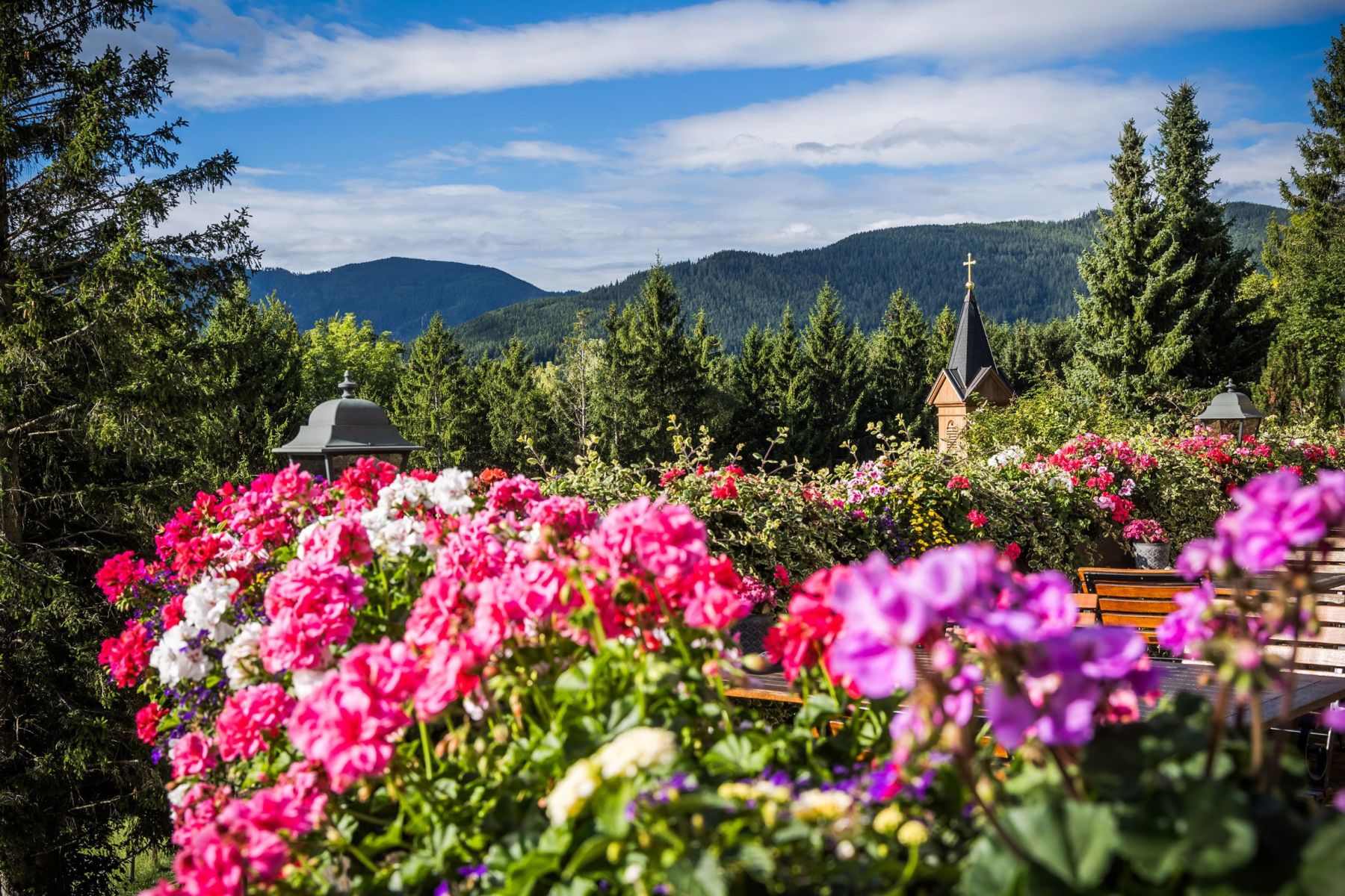Sommerliche Blumenpracht auf der Terrasse vom Hotel Knappenhof mit der Kapelle im Hintergrund.